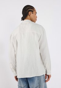 Chemise blanche texturée à manches longues et poignets boutonnés, dotée d'une coupe décontractée et d'un détail de dos yoke, associée à un jean bleu délavé.