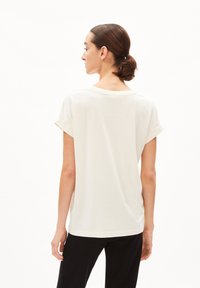 T-shirt à manches courtes et col rond en coton beige clair avec des manches retournées et une coupe décontractée, complété par une texture douce.