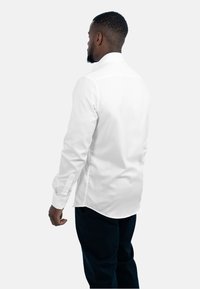 Witte blouse met lange mouwen, een opkraag met knopen, een gestructureerde stof, een getailleerde pasvorm en zijsplitten, gecombineerd met donkere broek.