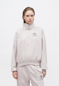 Felpa grigia chiara con zip, colletto alto, orlo a costine e logo ricamato che presenta un'icona di basket e il testo "PARIGI".