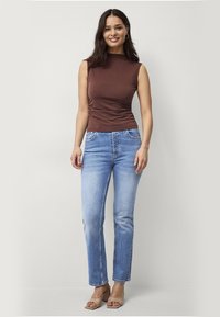 Bruine mouwloze top met zijsmarkering, gecombineerd met lichtblauwe rechte jeans en tan blokhak sandalen. Eenvoudig ontwerp, zachte stof.
