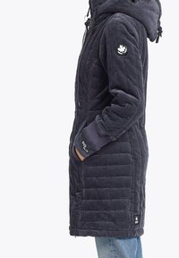 Mørkeblå corduroy jakke med quiltet design, justerbar hætte og ribbede manchetter. Har et logo patch på venstre ærme og sidelommer.