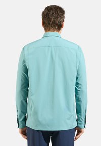 Turquoise long-sleeve shirt with a relaxed fit, textured fabric, and a back yoke. Features button cuffs and side slits for comfort.