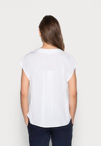 Witte blouse met korte mouwen en een relaxte pasvorm. Voorzien van een ronde halslijn en een iets langere achterkant, gemaakt van een gladde stof.
