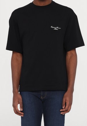 T-shirt en coton noir avec un col rond et des manches courtes. Présente un texte brodé blanc sur la poitrine gauche indiquant "Emporio Armani Milano."