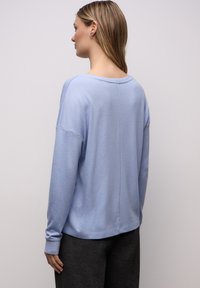 Jasnoniebieski sweter, lekka dzianina, luźny krój, szeroki dekolt, ściągacze na rękawach i u dołu, z delikatnym połyskiem. Widok z tyłu.