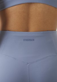 Light blue high-waisted leggings with a sleek texture, featuring an embossed "STRONGER" logo on the waistband and contrasting stitching.