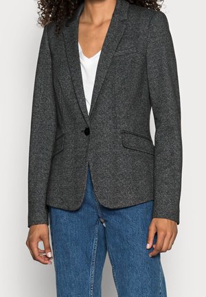 Blazer pied-de-poule en gris foncé, avec une fermeture à un bouton, deux poches avant et une coupe ajustée, associé à un jean bleu.