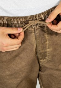 Braune Shorts aus glattem Stoff, mit einem elastischen Bund und Kordelzug. Sichtbare Nähte und Tascheninformationen.