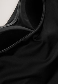 Sort stof med en glat tekstur, der viser en buet kant og fine syningsdetaljer, hvilket fremhæver fleksibilitet og blødhed.