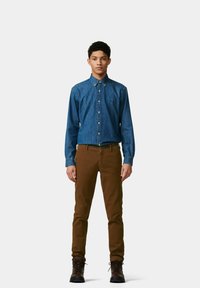Dunkelblaue Jeanshemd mit langen Ärmeln, Kragen und Logo; kombiniert mit braunen Hosen und dunklen Schnürstiefeln.