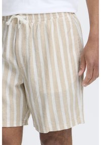 Shorts rayés beige et blanc en tissu léger avec une taille élastique et un cordon de serrage, dotés de poches latérales et d'une coupe décontractée.