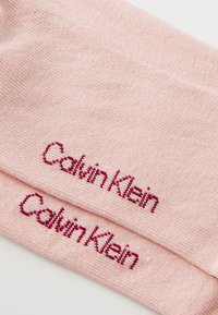 Heled roosa kootud kangas, millel on tume roosa niidiga broderitud Calvin Kleini logo kahel kattumisel kihil.