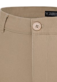 Jasno beżowe dopasowane spodnie charakteryzują się teksturowanym materiałem, z przodem na guziki z czterema dziurkami oraz stębnowanym szwem wzdłuż pasa.