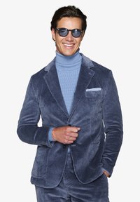 Mörkblå sammetsblazer med texturiserad ribbning, ihopparad med en ljusblå stickad polotröja. Accessoarer med mörka solglasögon.