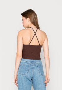 Top de alças finas com canelado castanho, combinado com jeans de ganga claros de cintura alta com bolsos nas costas.