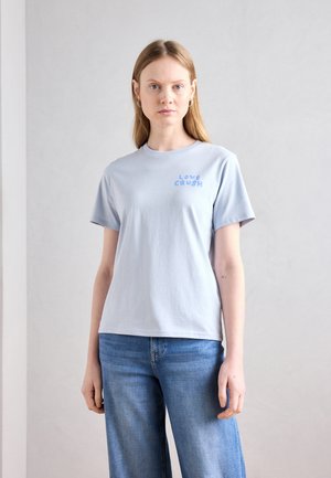 Hellblaues Baumwoll-T-Shirt mit kurzen Ärmeln, versehen mit "LOVE CRUSH" in blauer Schrift auf der Brust. Kombiniert mit blauen Jeans.