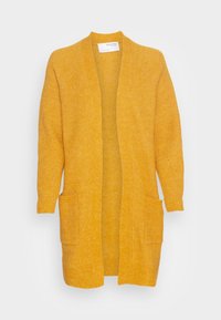Dlouhý hořčicově žlutý pletený cardigan s otevřeným předním dílem a dvěma předními našitými kapsami, vystavený na bílém pozadí.