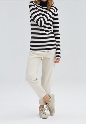 Zwart-wit gestreepte lange mouwtop met een col, gecombineerd met lichtgekleurde, tapered broeken en beige sneakers.