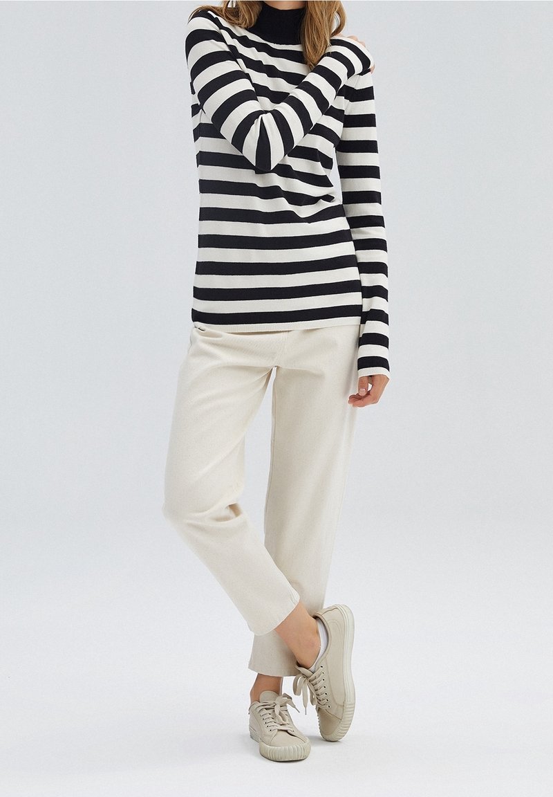 Schwarz-weiße gestreifte Langarmbluse mit Rollkragen, kombiniert mit hellen, taillierten Hosen und beigen Sneakers.