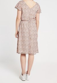 Robe à imprimé floral avec manches courtes volantées, dos en V, taille cintrée et jupe longueur genoux. Tissu léger aux teintes pastel. Baskets blanches.