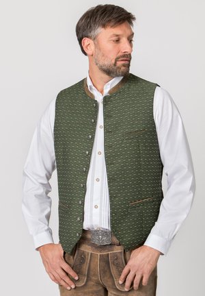 Mann trägt traditionelle bayerische Tracht mit grün gemusterter Weste, weißem Hemd und braunen Lederhosen mit dekorativer Gürtelschnalle.