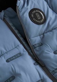 Šviesiai mėlyna pūkinė striukė su juodu užtrauktuku, logotipo pleistru ir pasikartojančiu "BAKER" tekstu ant audinio. Minkšta, lygi tekstūra.