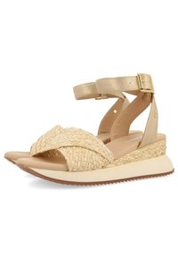 Sandalias tejidas beige con diseño de tiras cruzadas, correas metálicas en el tobillo y suela de cuña. Material texturizado y tacón de altura moderada.