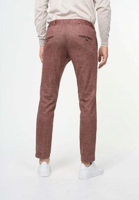 Pantalones marrones con textura, hechos de una tela tejida, que cuentan con dos bolsillos traseros con cremallera, diseño ajustado y se llevan con zapatillas blancas.