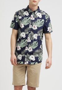 Košile s krátkým rukávem a zapínáním na knoflíky, tmavě modrý základ s tropickými zelenými listy a bílými květy s vínovými akcenty. Ležérní design.