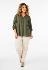 Chemise olive verte à col en V, manches trois-quarts, et pantalon beige. Tissu doux et coupe décontractée, associée à des bottes beiges claires.