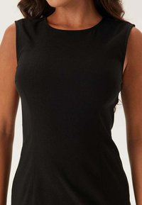 Svart ärmlös klänning med rund halsringning. Jämn tyg med en figurnära silhuett och subtila sidsömmar. Klassisk design och mångsidig stil.
