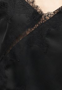 Μαύρο σατέν ύφασμα με περίτεχνη δαντέλα με σχέδιο λουλουδιών κατά μήκος της V-σχήματος λαιμόκοψης και της λεπτομέρειας στο στήθος.