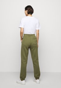 Olivegrüne Sweatpants mit elastischem Bund und gerippten Bündchen, versehen mit einer einzelnen Gesäßtasche. Kombiniert mit einem schlichten weißen T-Shirt mit Rundhalsausschnitt.