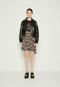 Casaco de couro preto sobre um top curto gráfico, combinado com uma saia de estampa de leopardo com babados. Completo com sandálias pretas de plataforma.