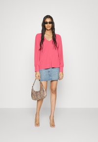 Blusa rosa de mangas longas com decote em V, saia mini de denim azul e uma bolsa de textura de pele de cobra. Sandálias de salto transparente completam o visual.