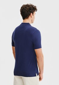 Granatowa koszulka polo z krótkimi rękawami, gładka w dotyku, z bocznymi rozporkami u dołu. Zaprojektowana z klasycznym kołnierzykiem oraz detalem w postaci karczku z tyłu.
