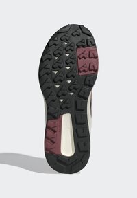 Shoe outsole featuring a black rubber base with multidirectional lugs for traction and accents of maroon and beige for added detail.