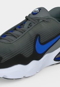 Γκρι αθλητικό παπούτσι Nike Air Max με μπλε λογότυπο, μαύρες λεπτομέρειες, γκρι κορδόνια και λευκή σόλα, εμφανιζόμενο σε κοντινή λήψη.