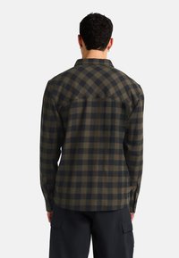 Chemise à manches longues à carreaux dans des tons de vert foncé et noir. Fabriquée en tissu doux, elle possède un ourlet arrondi, des poignets à boutons et un col classique.