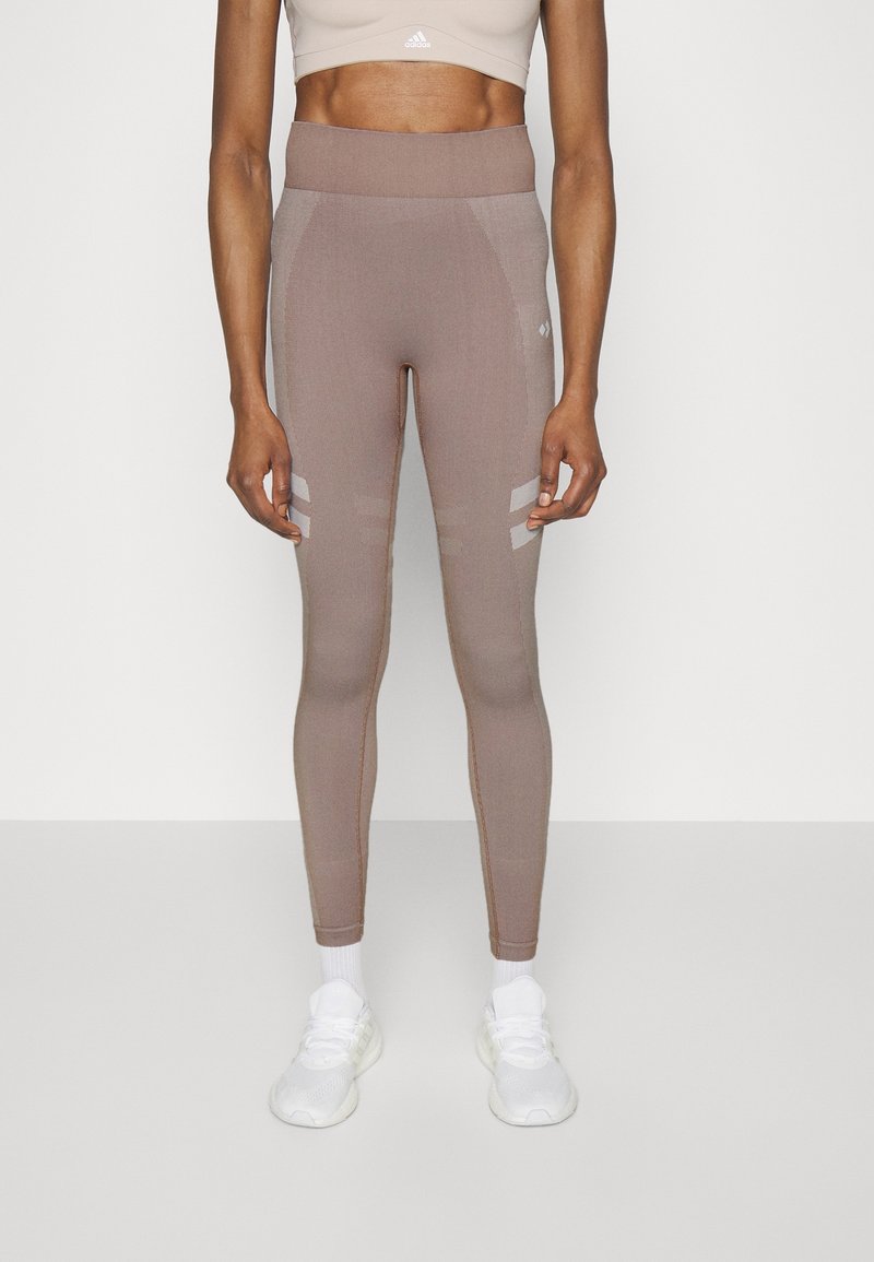 Leggings a vita alta, aderenti, in un materiale tricot marrone chiaro con pannelli testurizzati e sottili strisce, abbinati a scarpe da ginnastica bianche.