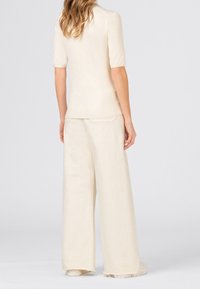 Svetle béžové pouzdrové tričko s krátkým rukávem, zkombinované s volnými béžovými kalhotami. Měkká látka s minimální texturou a pružnými detaily.