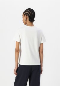 T-shirt en coton blanc avec une coupe décontractée, des manches courtes et un col rond. Tissu lisse, ourlet droit et design minimaliste.