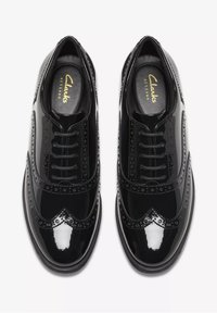 Schwarze Lacklederschuhe mit aufwendigen Brogue-Details, runder Spitze und sechs Ösen für die Schnürsenkel. Weiche Fütterung und gepolsterte Innensohle.