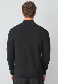 Schwarzer Strickpullover mit geripptem Kragen, langen Ärmeln und einer glatten Textur. Auf der Rückseite sind keine sichtbaren Muster oder Logos.