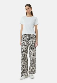 T-shirt bianco in cotone con maniche corte abbinato a pantaloni beige a gamba larga con stampa leopardata nera e cintura elastica.