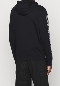 Sudadera de marina hecha de una mezcla de algodón. Cuenta con un bolsillo canguro, dobladillo acanalado y estampado del logo en blanco a lo largo de la manga derecha.