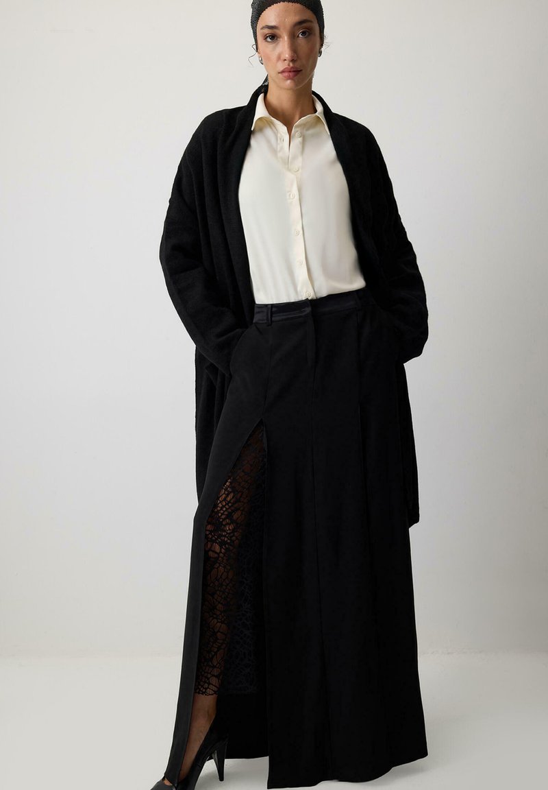 Melnas garas svārku ar mežģīņu iestrādi, apvienoti ar baltu pogājamā krekla un melnu džemperi, kuram ir brīva piegriezuma un sānu šķēlums.