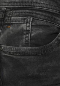 Svarta denimjeans har en bakficka med distinkt sömnad och en liten orange detalj, vilket visar en texturerad tygytan.