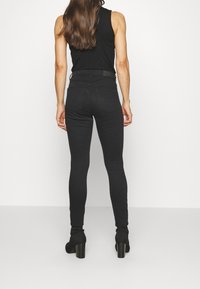 Jeans ajustados negros con cintura alta, textura suave y diseño de cinco bolsillos. Combinados con una blusa sin mangas negra y botas de tacón negras.